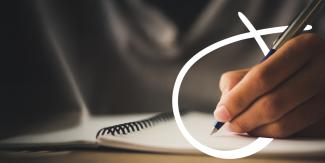 Close-up of a hand writing with a pen on a spiral-bound notebook, with a white curved graphic element overlaid on the image.