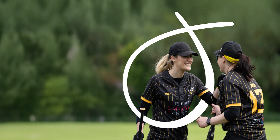 Two people from Lisburn Softball Team wearing black and yellow sports uniforms standing on a grassy field, one with number 17 visible