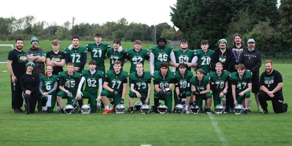 Belfast Trojans youth team group photo with players in green uniforms and coaches on a grassy field