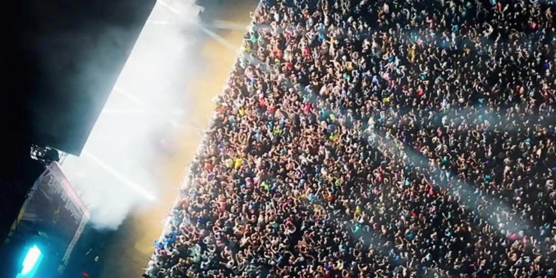 Thousands of people gathered at an outdoor concert, illuminated by stage lights at night.